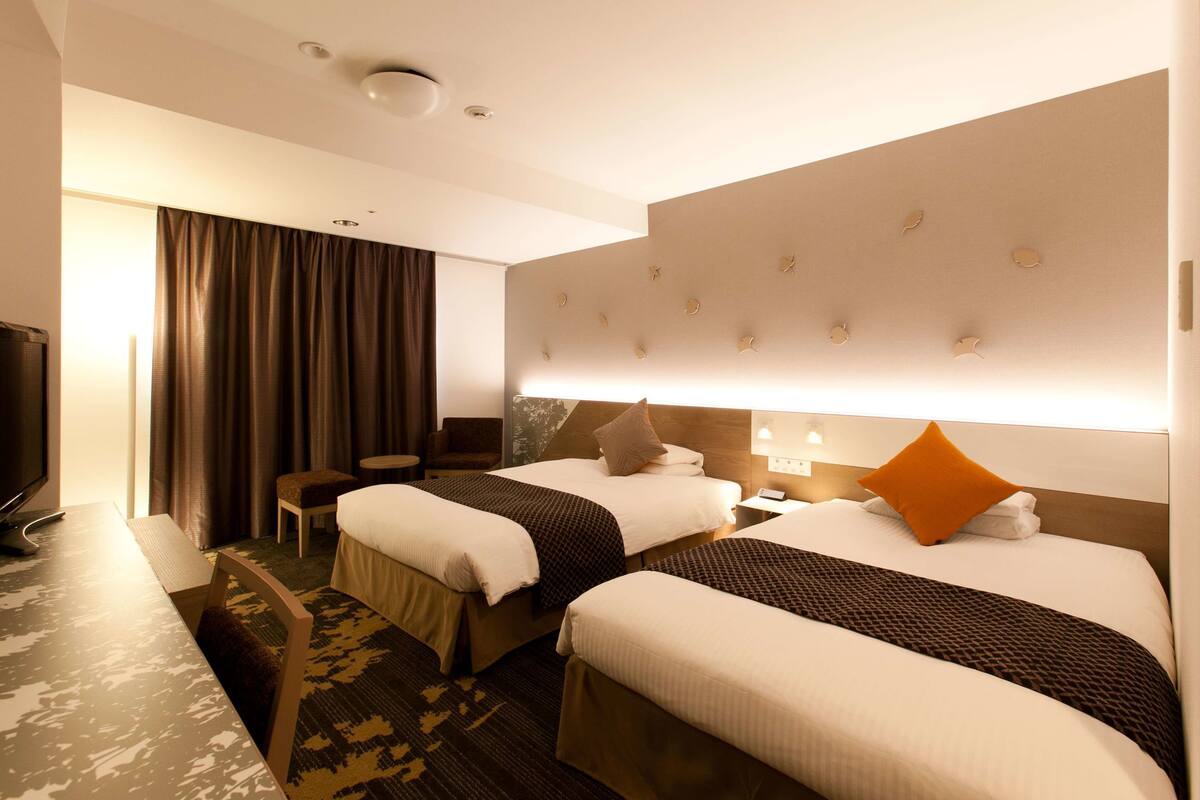 A hotel room with two beds, a desk, a chair, and a television.