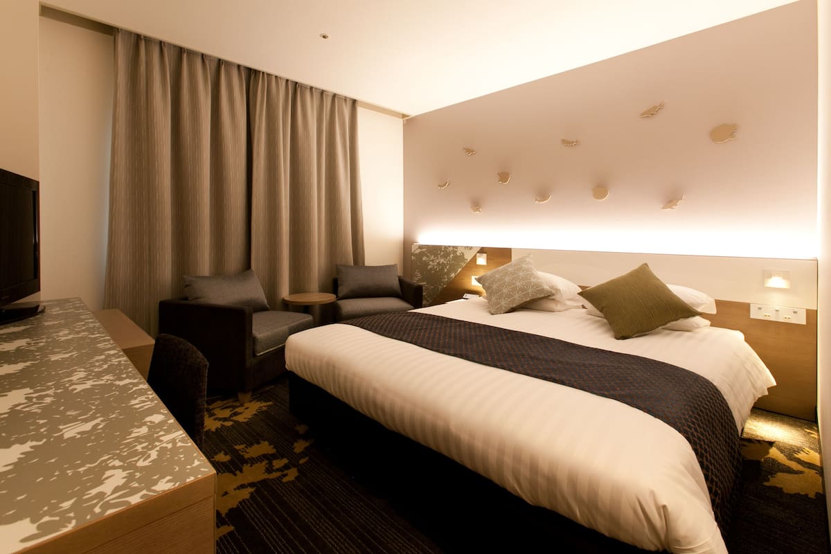 A hotel room with a large bed, a desk, a chair, and a television.