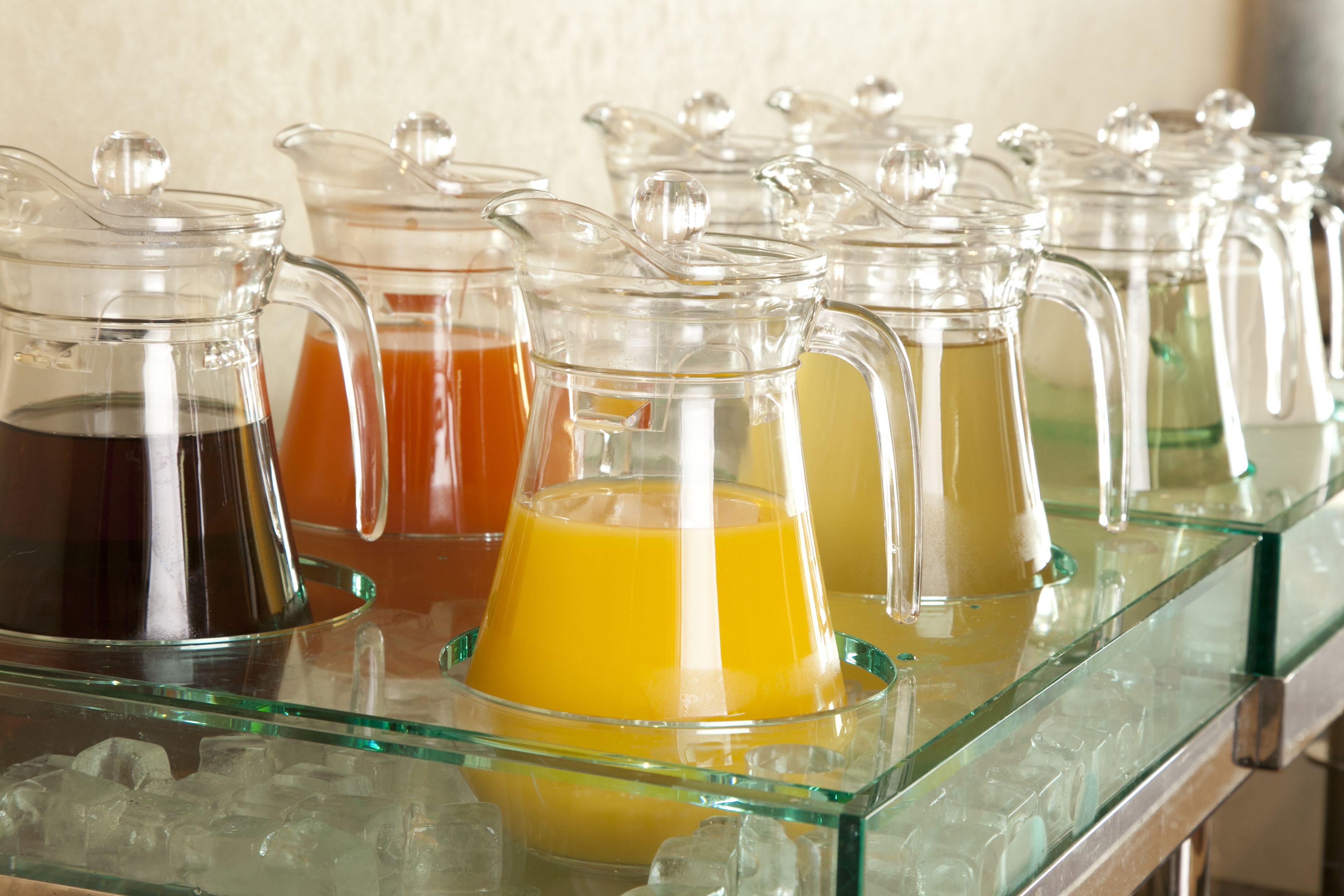 A row of glass dispensers with different colored beverages on a glass shelf.