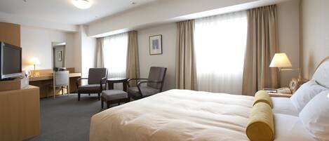 A hotel room with a large bed, a desk with a chair, a television, and a lamp.