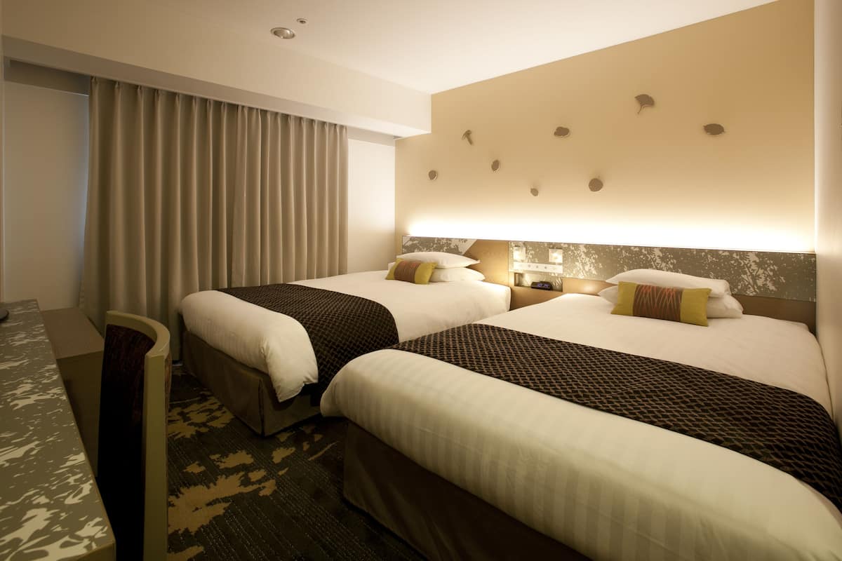 A hotel room with two beds, a desk, and a large window with curtains.