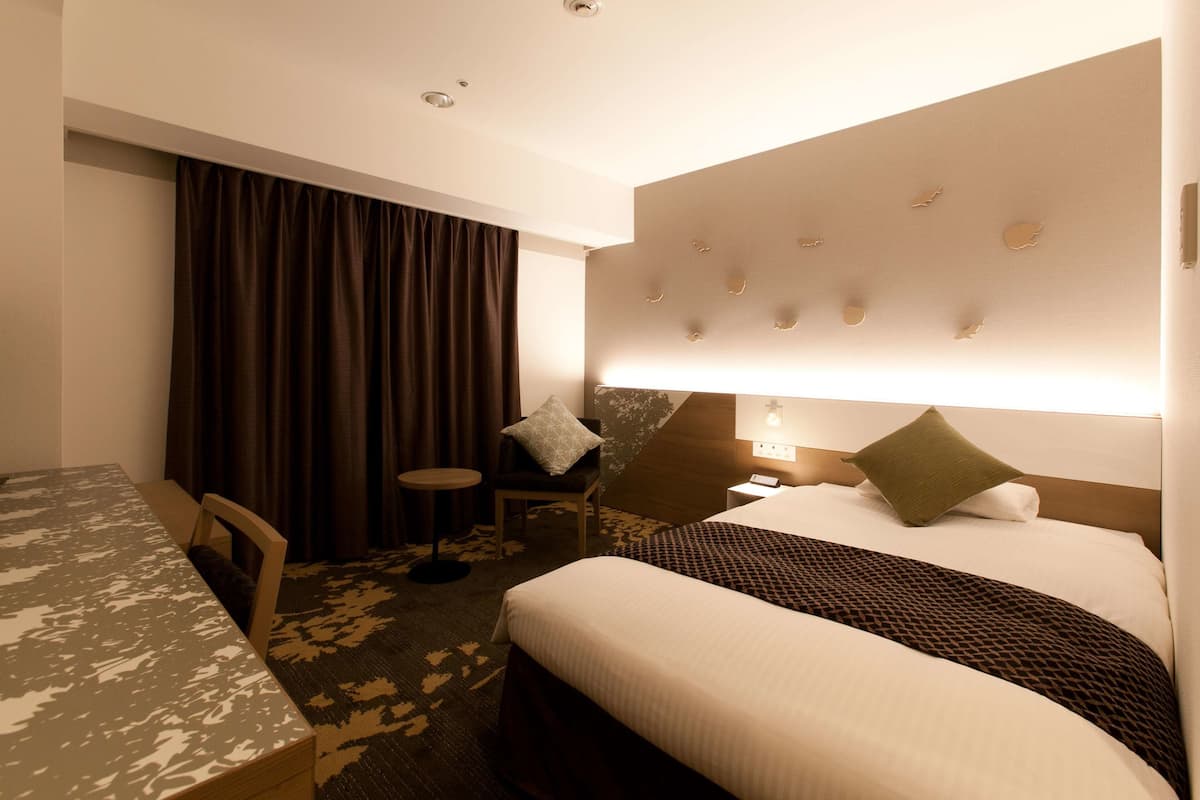 A hotel room with a bed, a desk, a chair, and a small table.