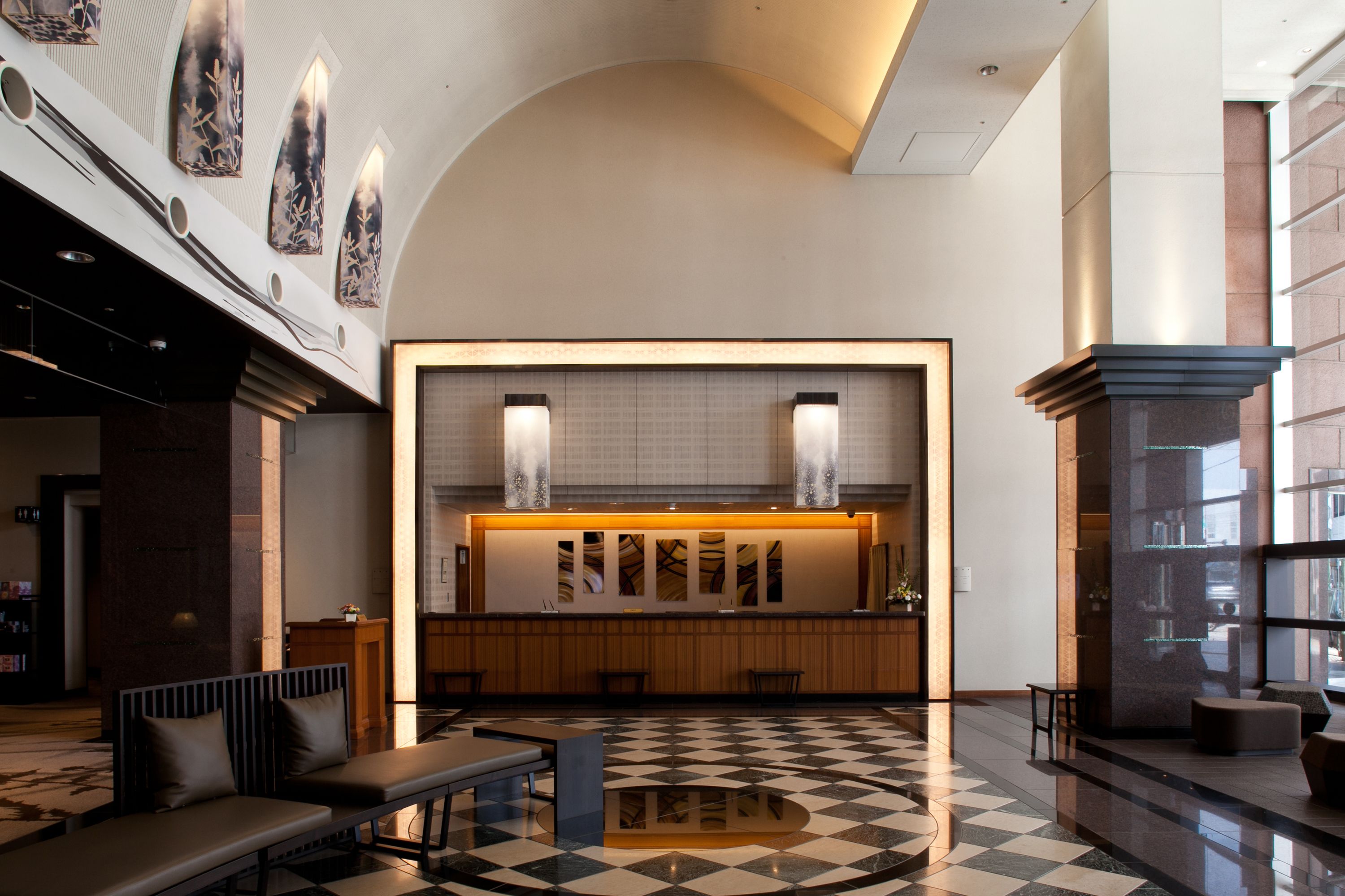 A lobby with a checkered floor, a reception desk, seating area, and a staircase.