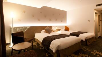Una habitación de hotel con dos camas, una silla, una mesita y una lámpara fijada a la pared.