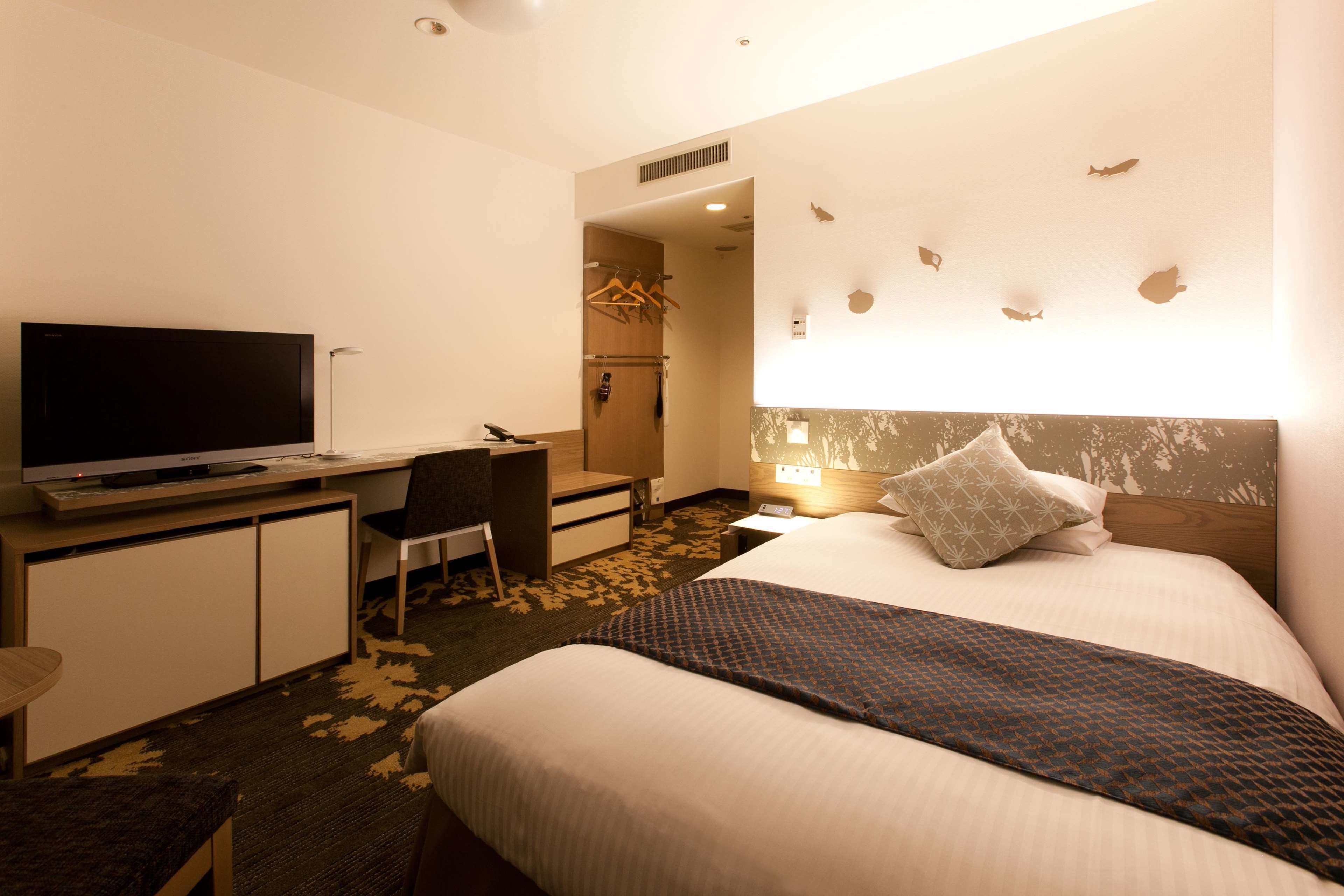 Een hotelkamer met een bed, een bureau met televisie, een stoel, een garderobe en een muur met visdecoraties.