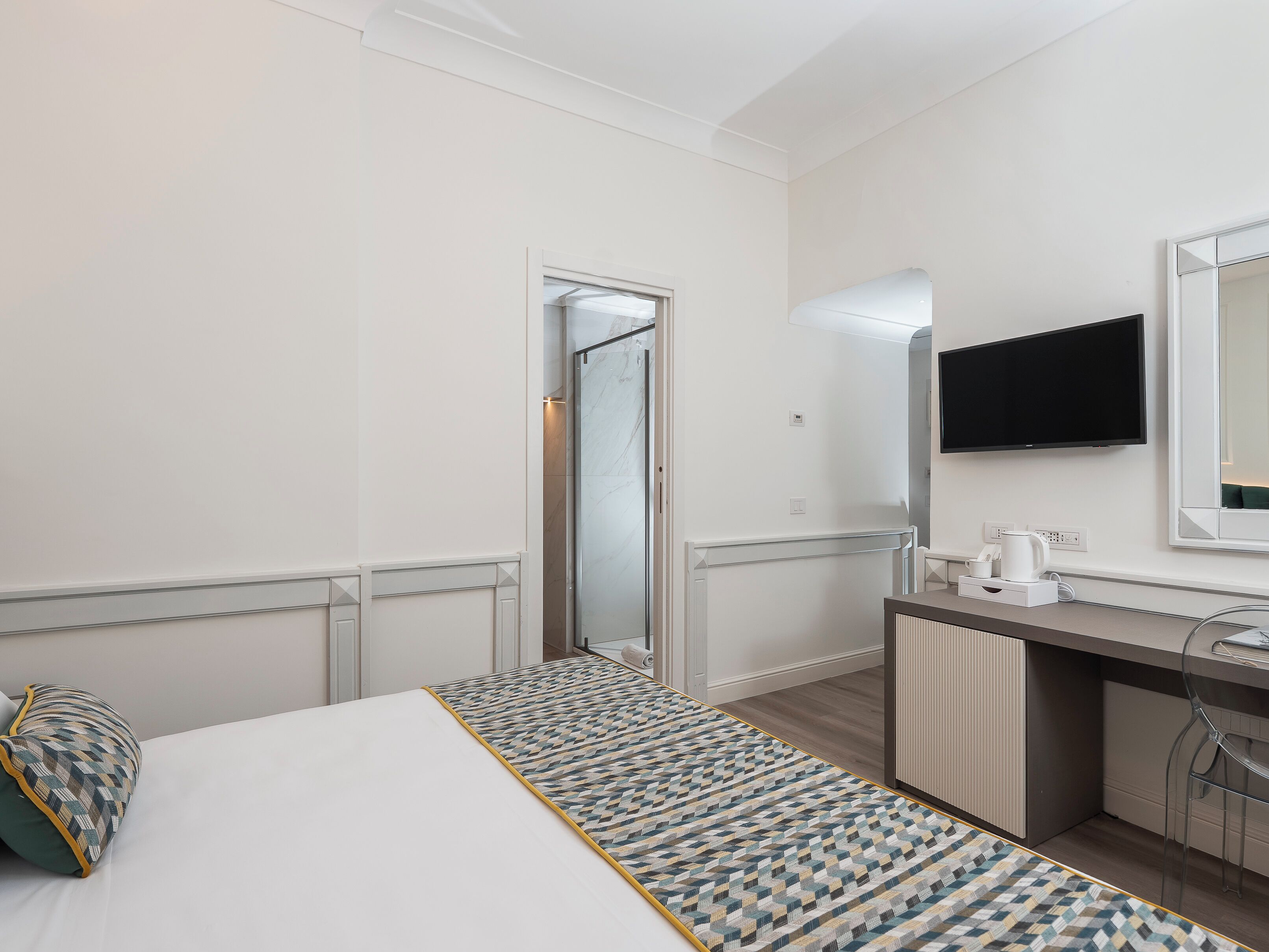 A hotel room with a bed, a desk, a mirror, a TV, and a bathroom visible through an open door.