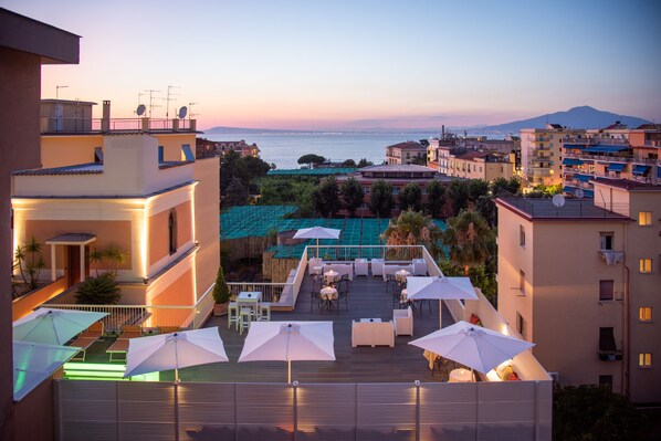 Terraza en la azotea con mobiliario exterior y sombrillas, con vistas a la ciudad y al mar.