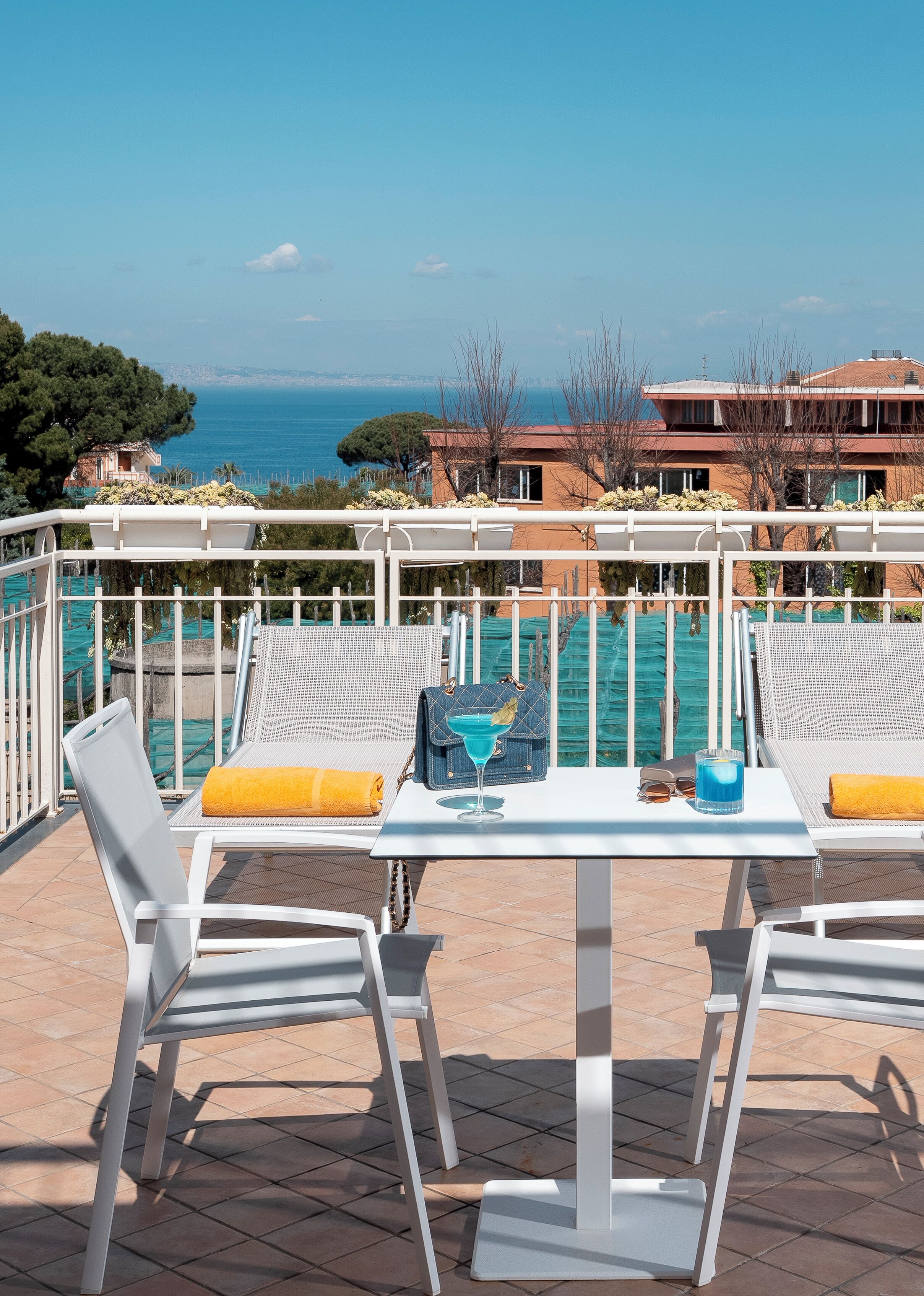 A terrace with white chairs and a table, overlooking a pool and the sea.