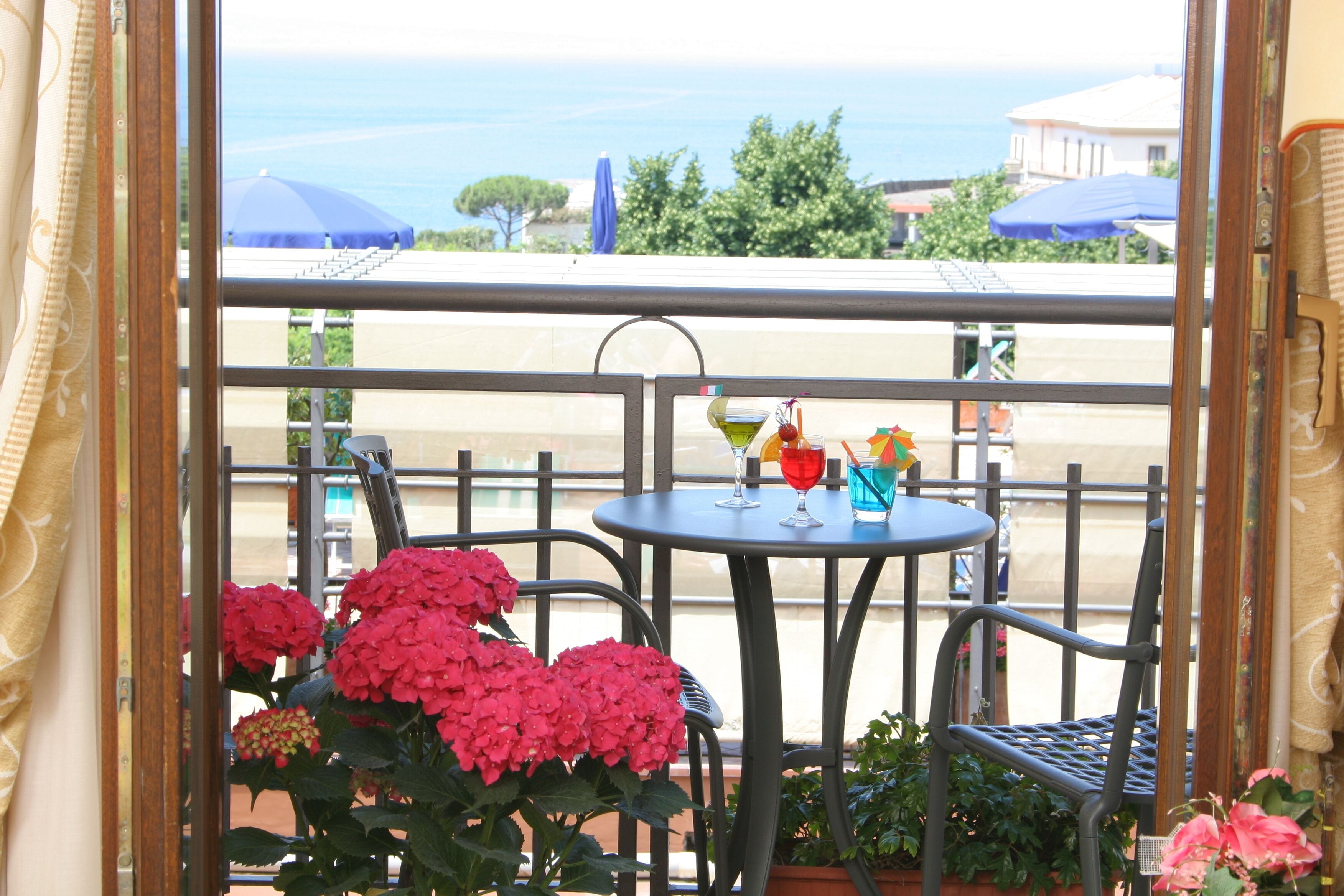 A balcony with a table and chairs, potted plants, and a view of the sea.
