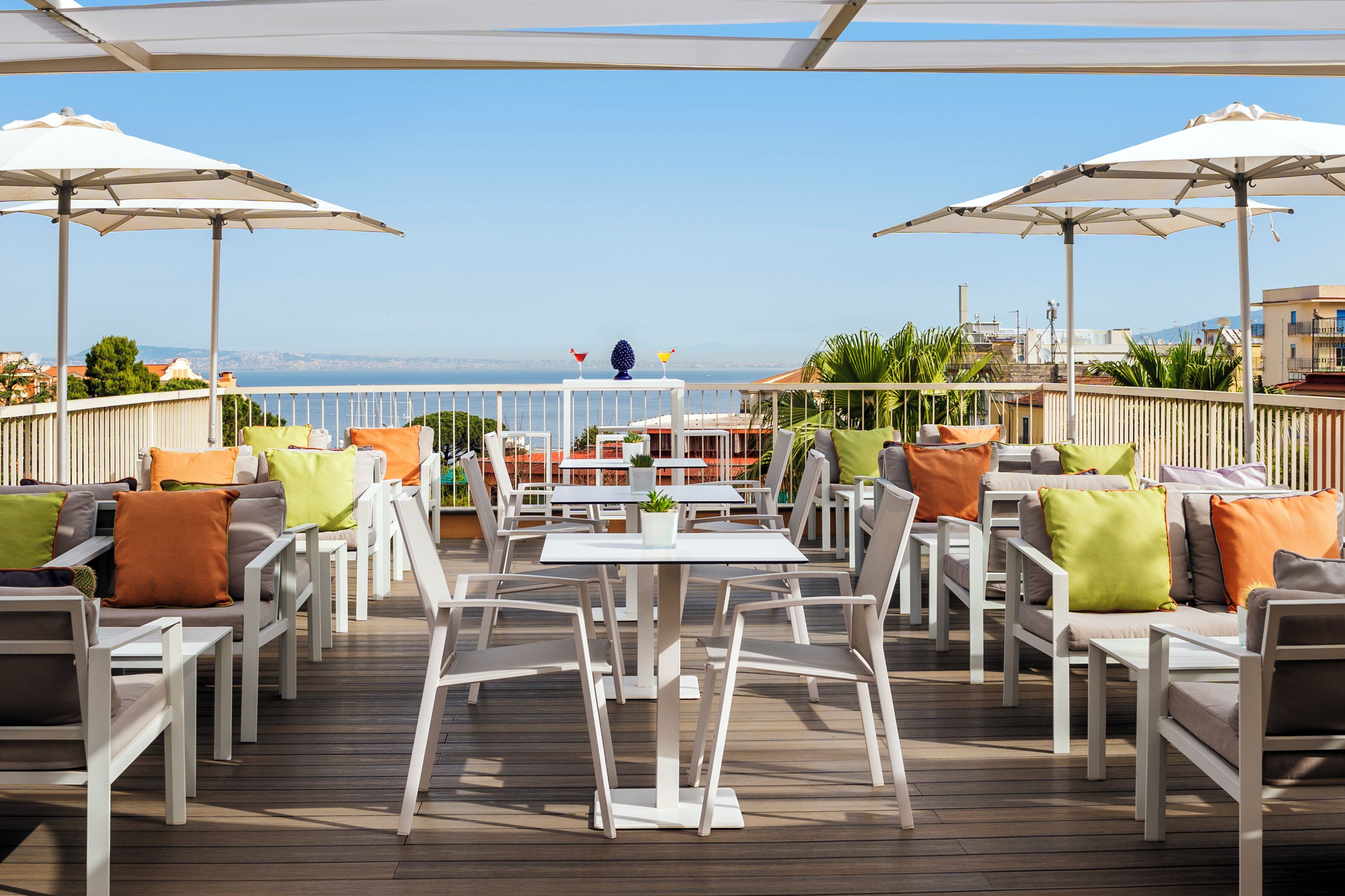 An outdoor patio with white furniture, umbrellas, and a view of the sea.