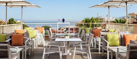 An outdoor patio with white furniture, umbrellas, and a view of the sea.