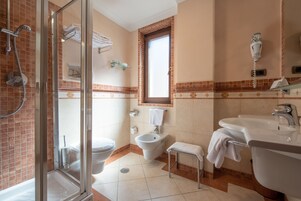 Un baño con cabina de ducha de vidrio, un bidé, un lavamanos y una ventana.