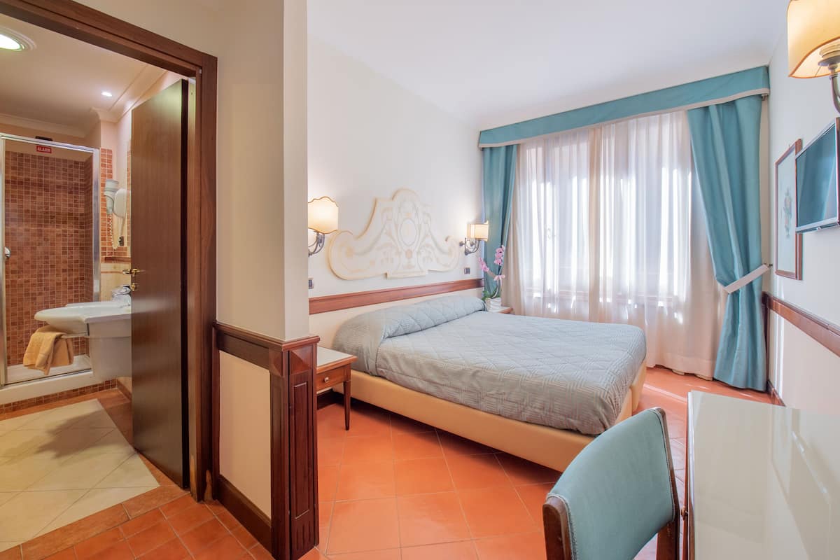 Une chambre d’hôtel équipée d’un lit, d’un bureau, d’une chaise, d’un miroir et d’une salle de bain avec un lavabo et des toilettes.