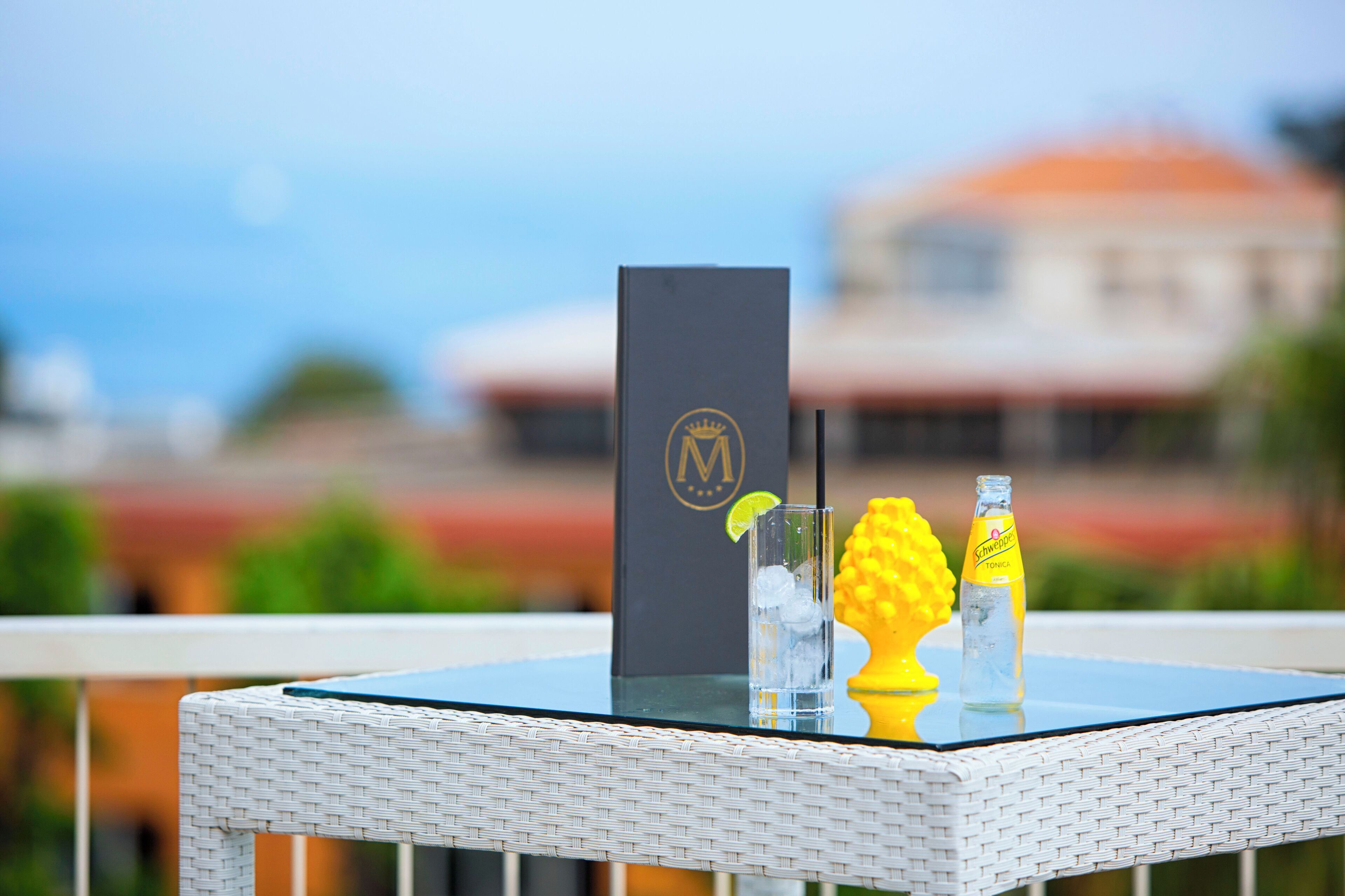 Une table en verre sur laquelle se trouvent une bouteille d’eau tonique Schweppes, un quartier de citron vert et un verre à cocktail rempli de glaçons.