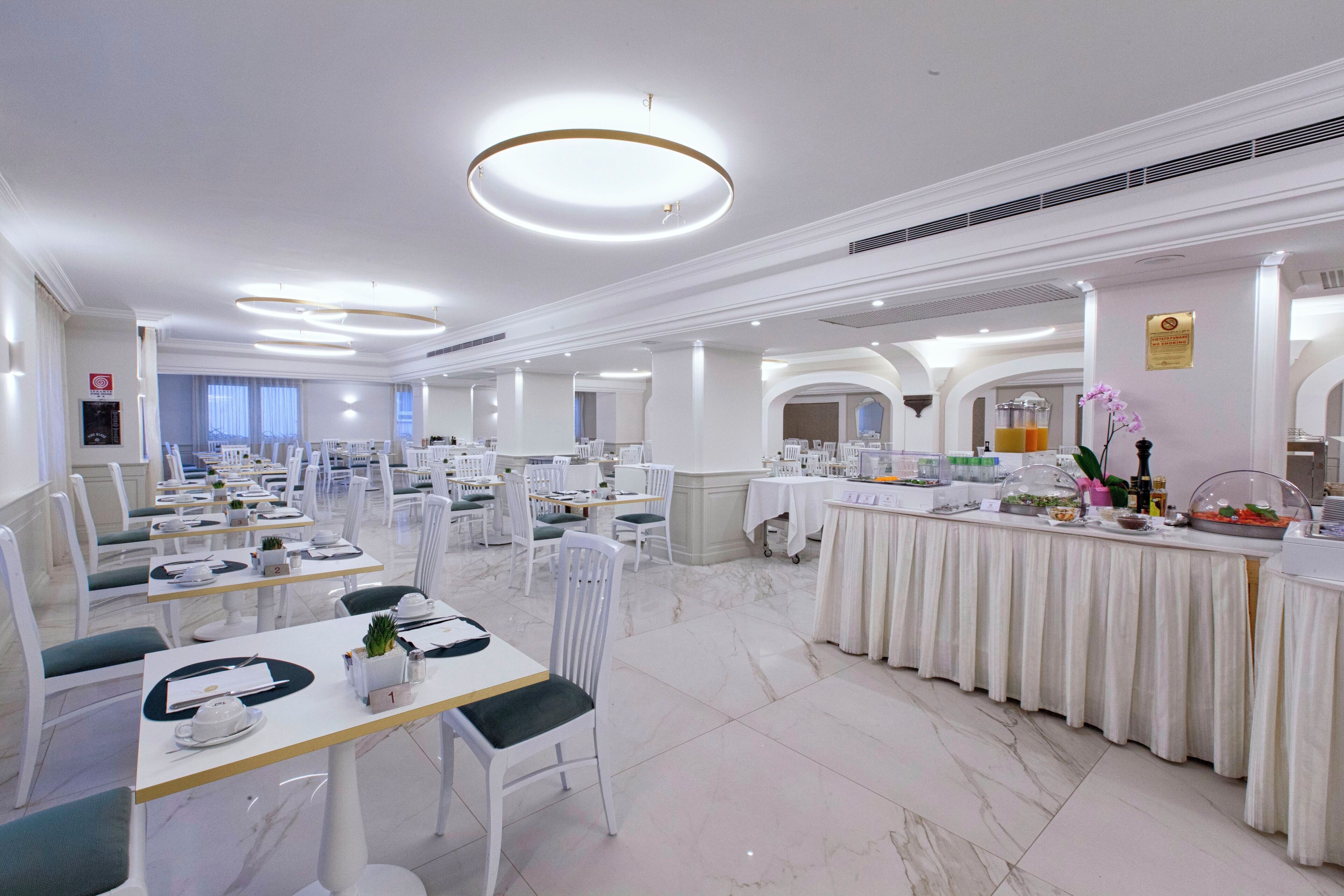 Un amplio comedor con varias mesas y sillas, una barra de buffet y una lámpara de araña moderna.