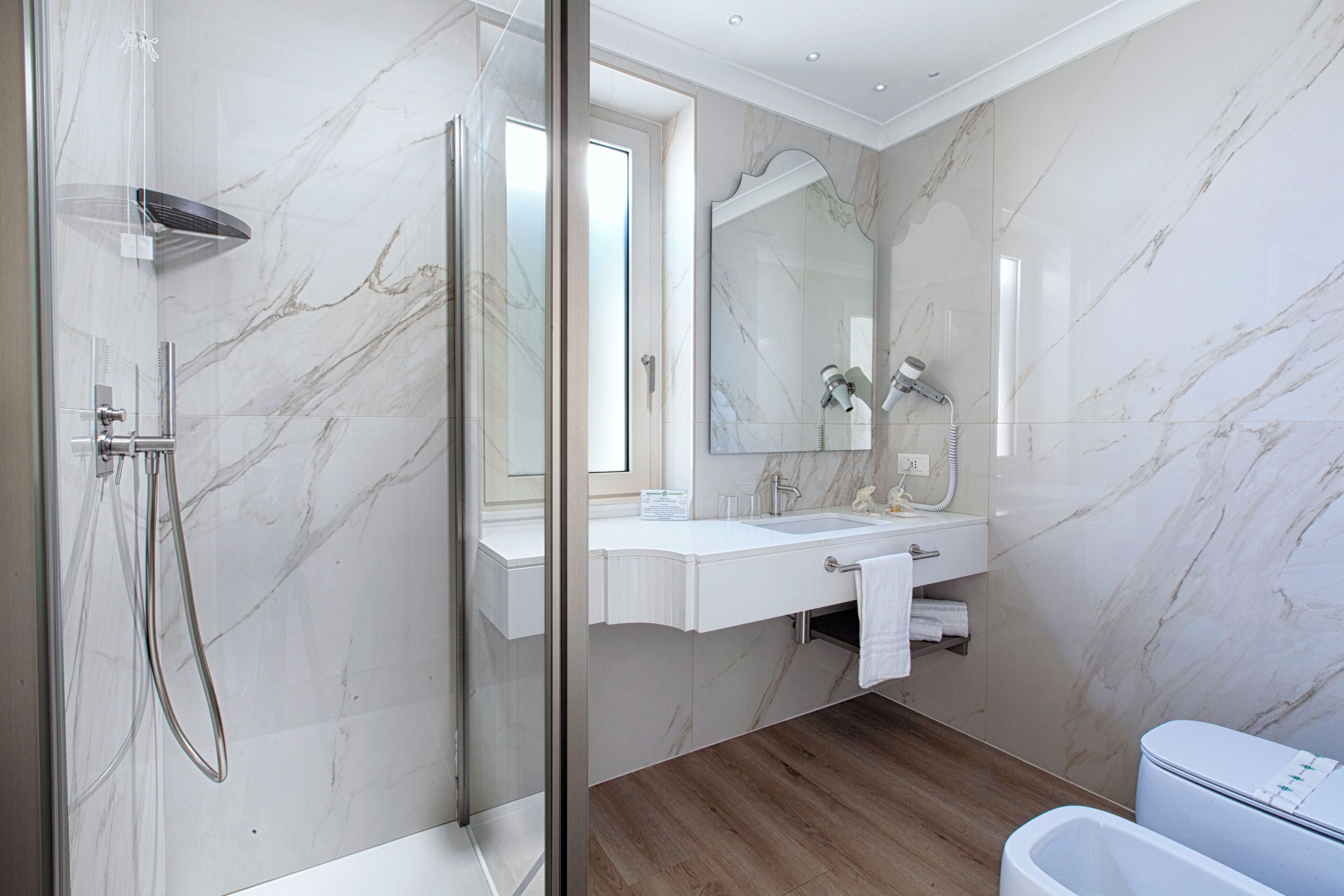 Un baño moderno con ducha de vidrio, lavabo de mármol blanco y un espejo grande.