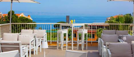 Una terraza con mobiliario blanco, incluyendo sillas y mesas, con vista al litoral.