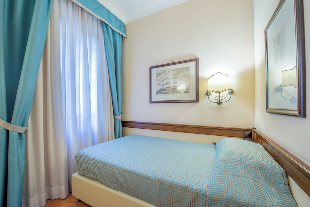 Une chambre d’hôtel avec un lit, des rideaux, une lampe fixée au mur et un tableau encadré.