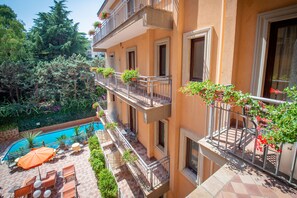 Un edificio de varios pisos con piscina, mobiliario exterior y balcones con plantas en macetas.