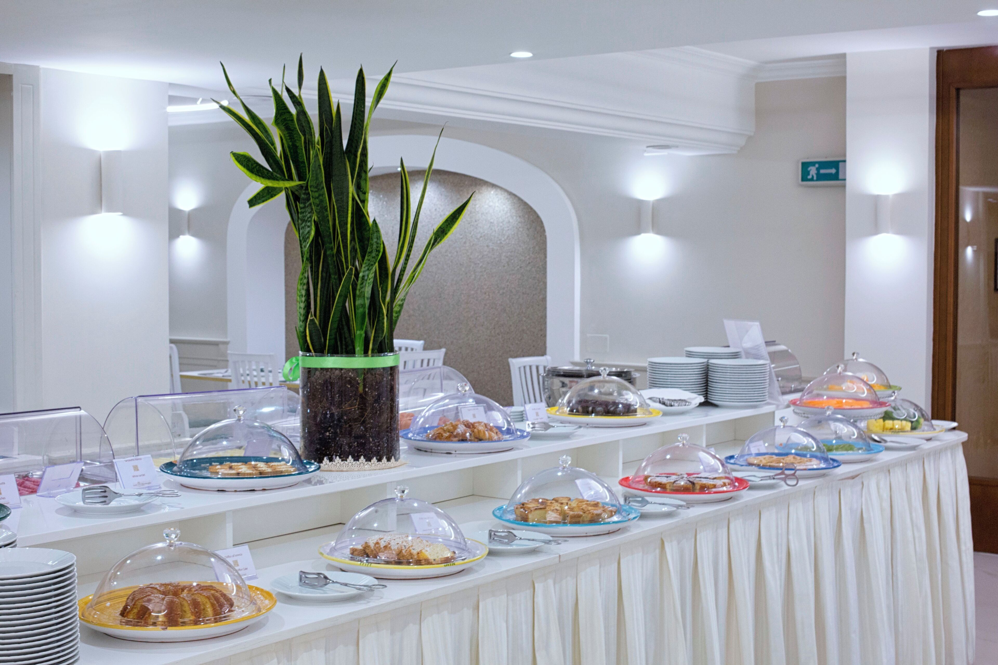 A buffet table with various food items covered with glass domes, a potted plant, and a sign indicating an exit.