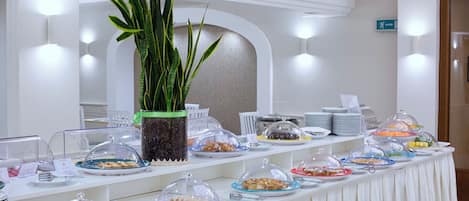 A buffet table with various food items covered with glass domes, a potted plant, and a sign indicating an exit.