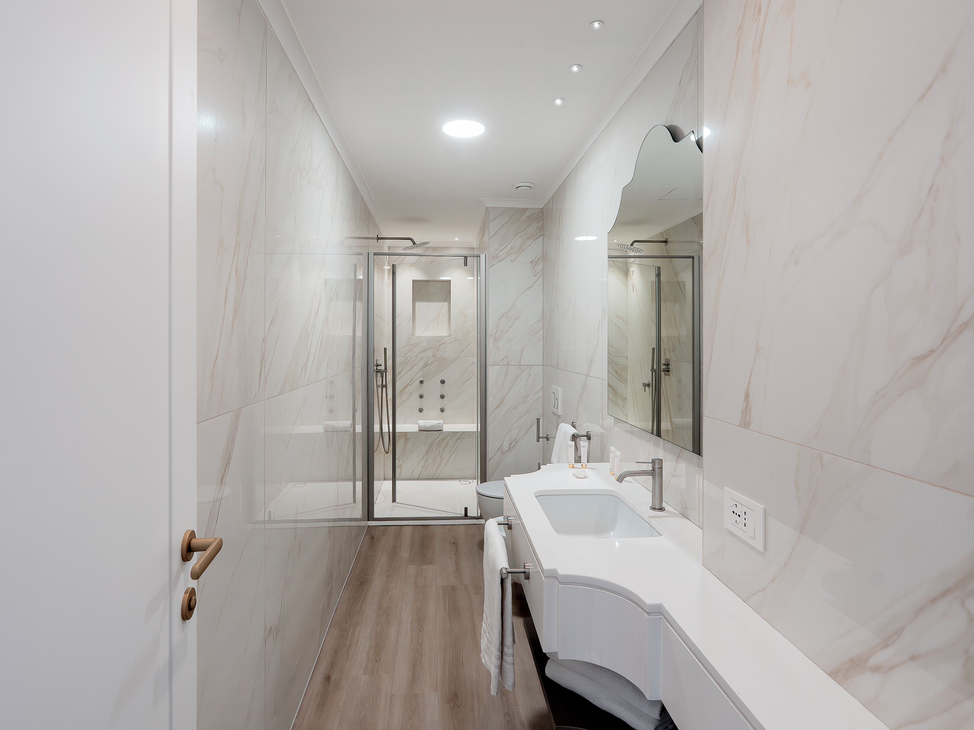 Uma casa de banho moderna com chuveiro envolto em vidro, toucador branco com lavatório e um espelho grande.