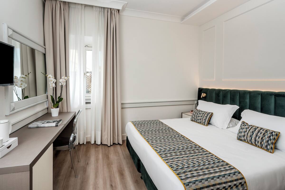 Une chambre d’hôtel avec un lit, une table de chevet, une télévision et une fenêtre avec des rideaux.