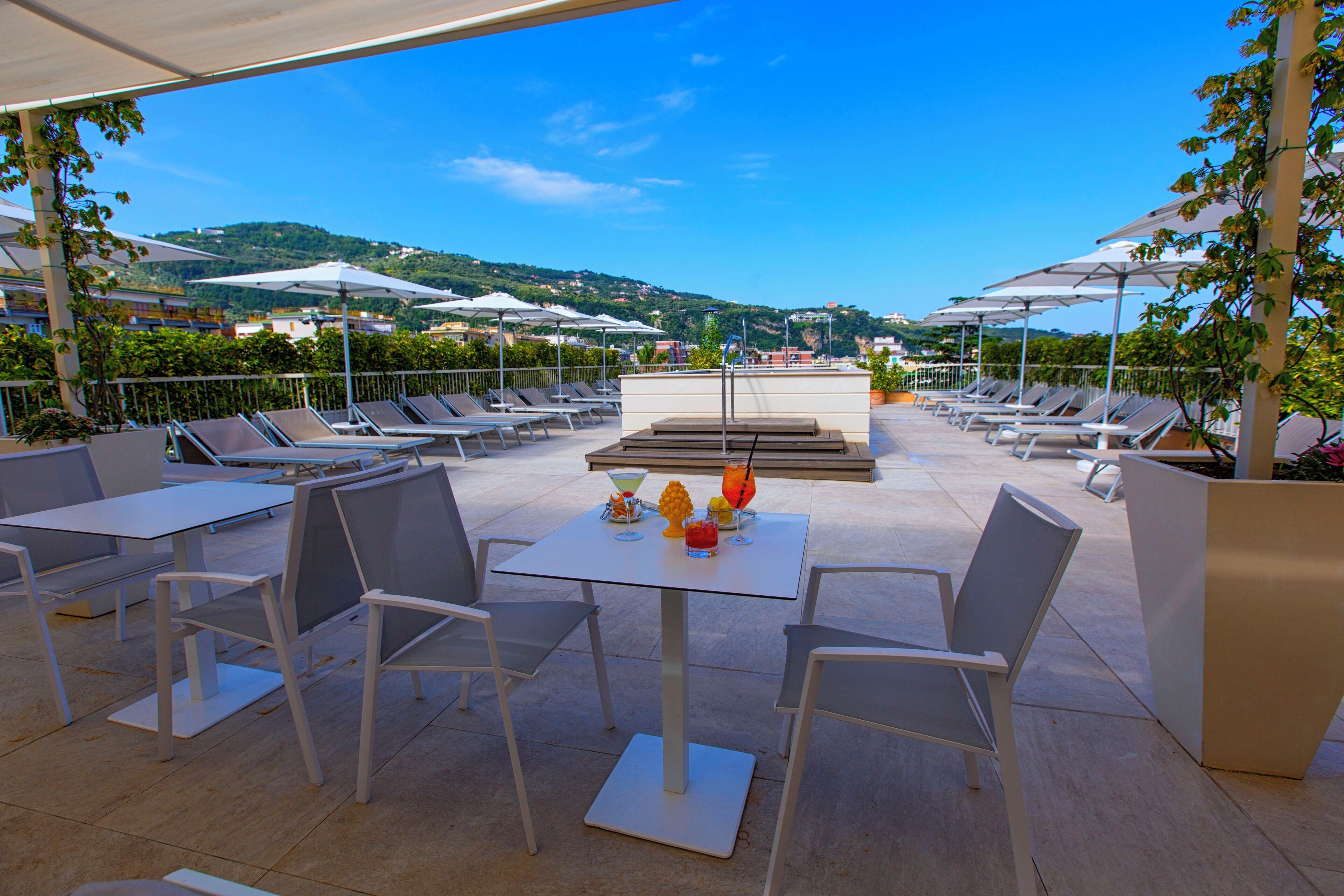 Un espace extérieur aménagé avec des tables, des chaises, des parasols et une vue sur les collines.