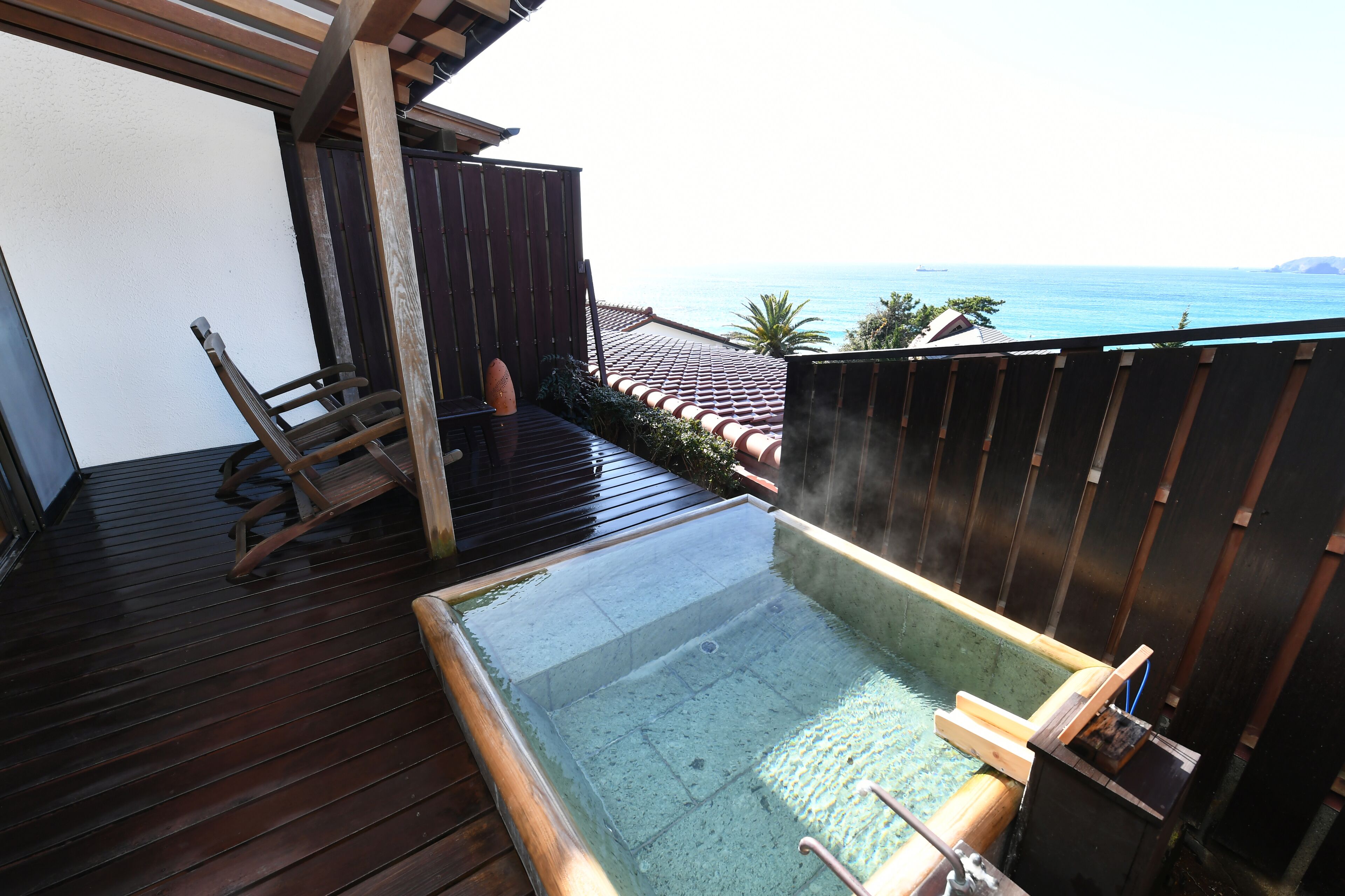 A wooden deck with a hot tub, a wooden chair, and a view of the sea.