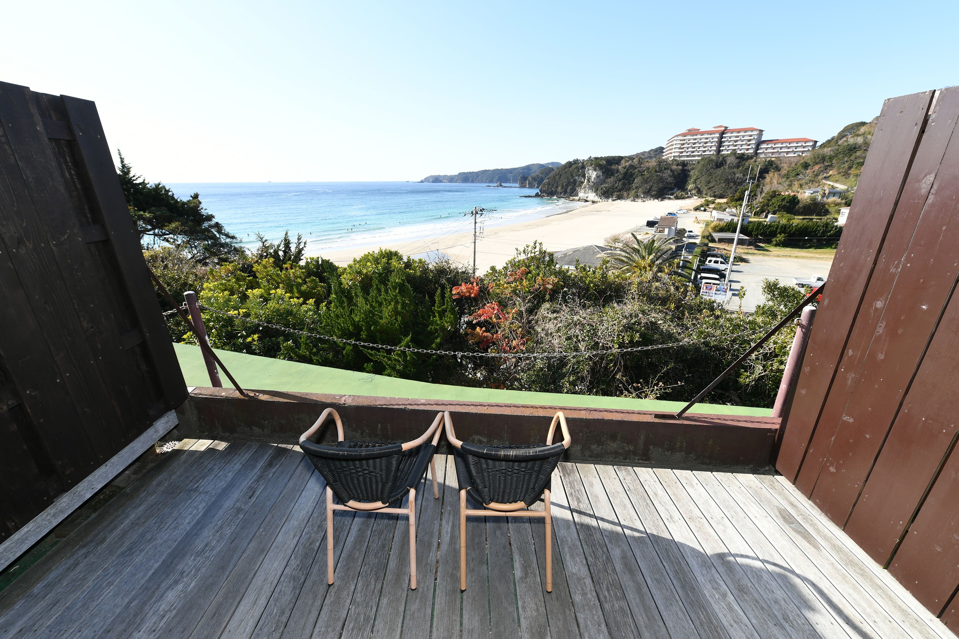 En balkon med to fletstole med udsigt over stranden.