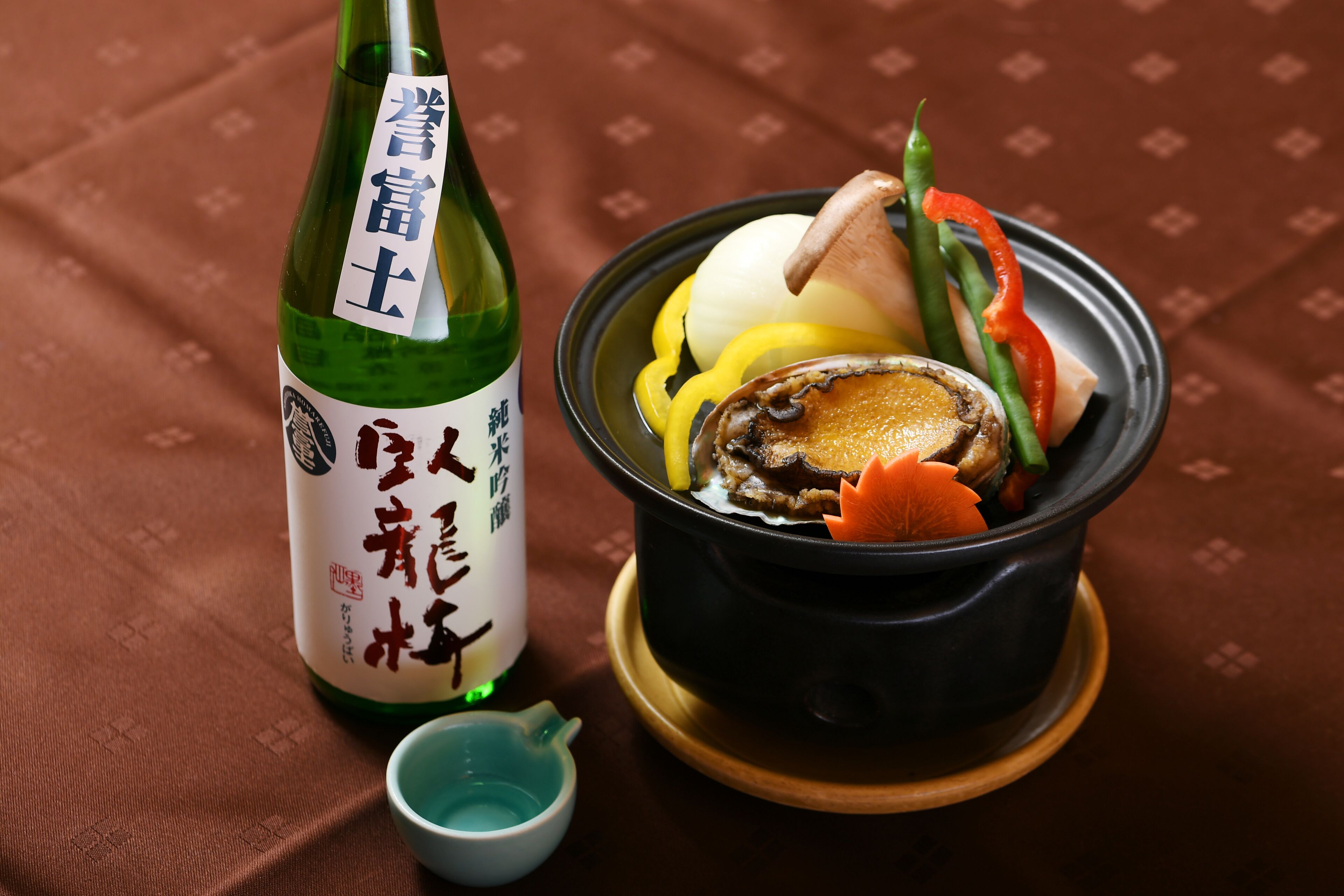 A bottle of sake and a bowl of food with vegetables and a piece of meat.