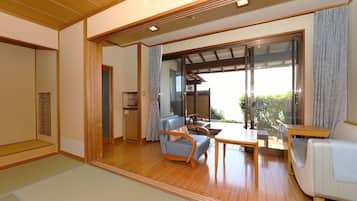 Una tradizionale stanza in stile giapponese con pavimento in tatami, una porta scorrevole in vetro che dà su uno spazio esterno e un tavolino in legno con sedie.