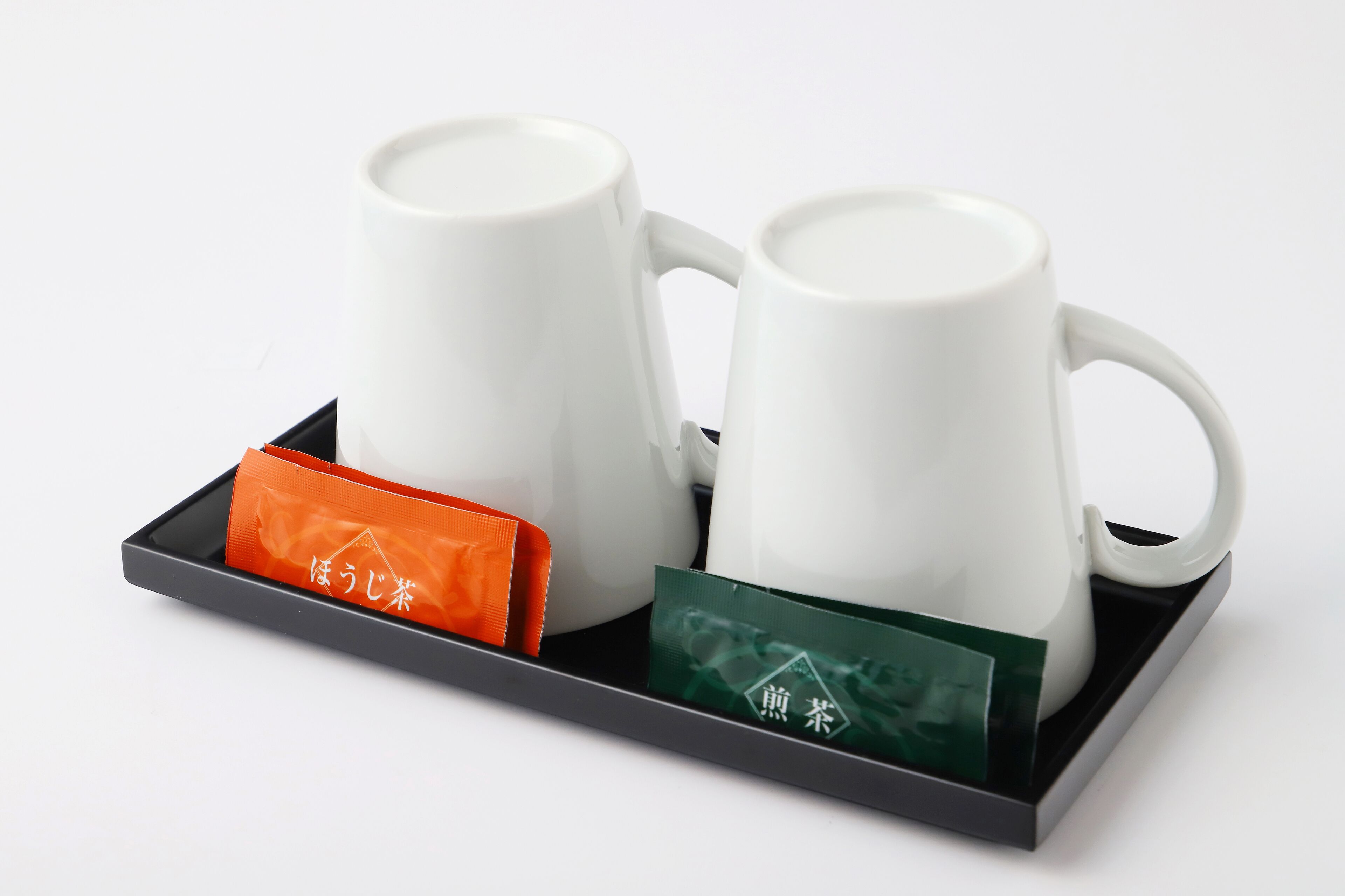 Dos tazas de cerámica blanca sobre una bandeja con dos bolsitas de té, una naranja y una verde.