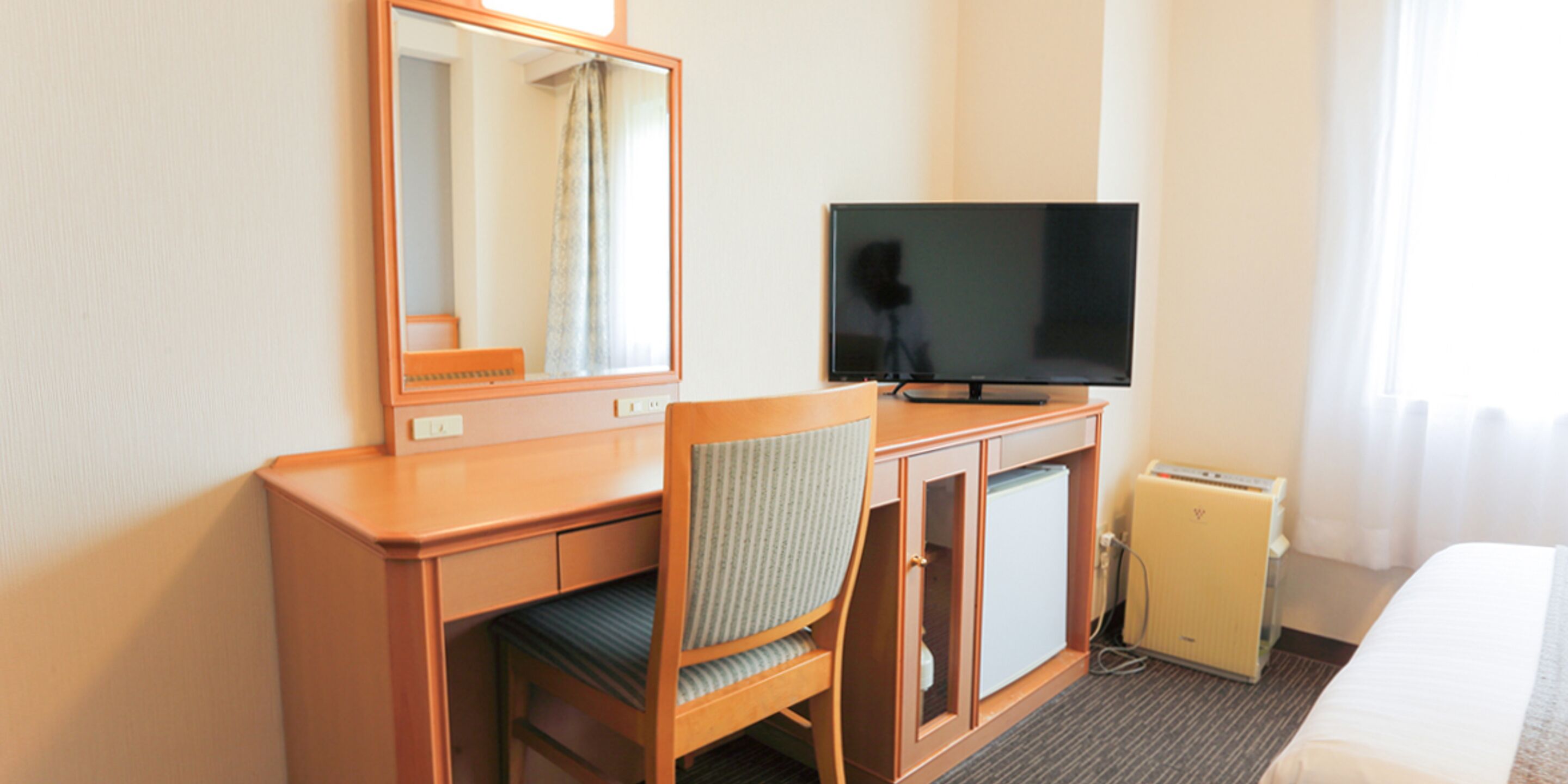 A hotel room with a wooden desk, a television, a small refrigerator, and a bed.