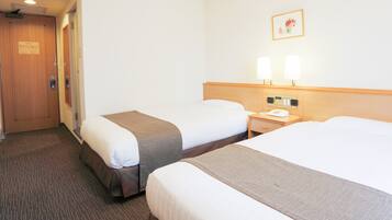 A hotel room with two beds, a wooden door, a bedside table with a phone, and a wall-mounted lamp.