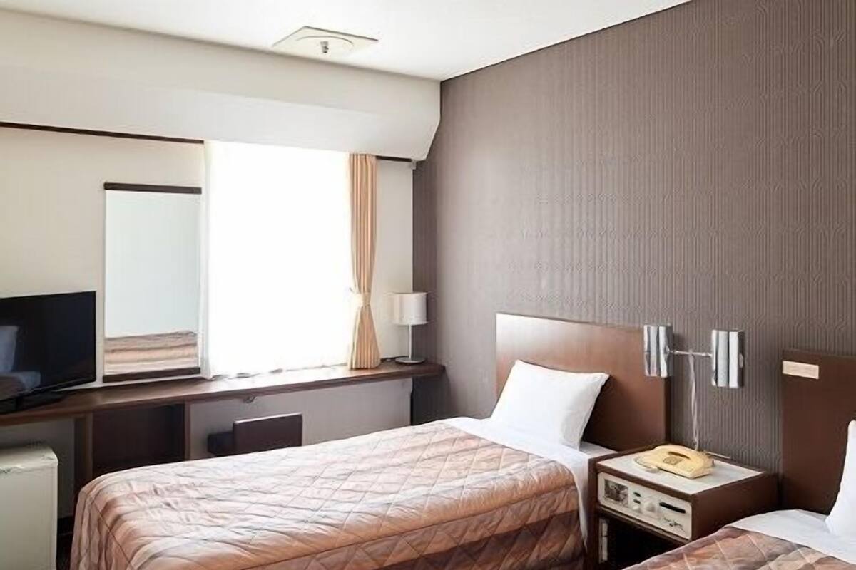 A hotel room with two beds, a desk, a television, and a bedside table with a lamp.