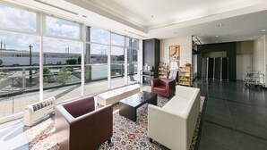 Eine geräumige Lobby mit großen Fenstern, eine Sitzecke mit Sofas und einem Couchtisch, ein Bücherregal und ein Empfangstisch.