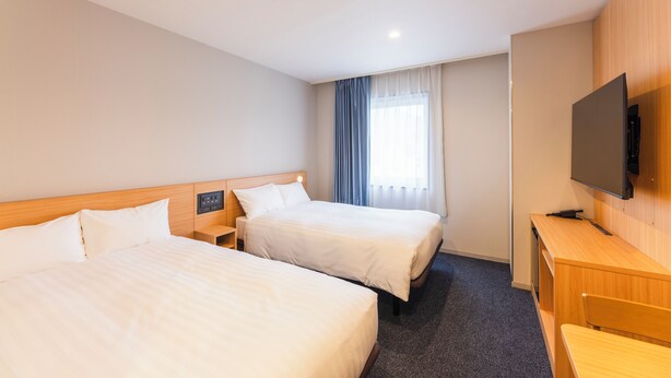 Ein Hotelzimmer mit zwei Betten, einem Schreibtisch, einem Fernseher und einem fensterbepflanzten Fenster.