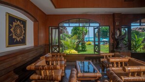 A lobby with wooden furniture, a large decorative mirror, and a view of a tropical garden and pool. - Aloha Resort (Koh Samui)
