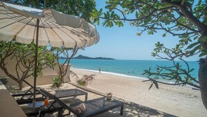 A beachside lounge with a large umbrella, lounge chairs, and a view of the ocean. - Aloha Resort (Koh Samui)