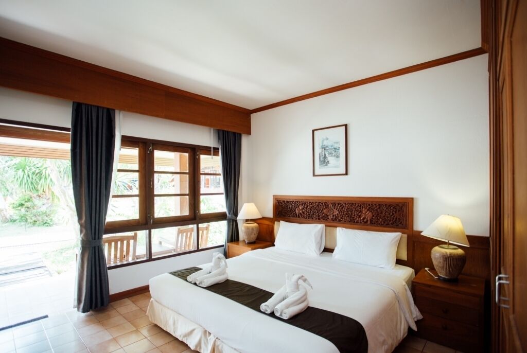 Habitación de hotel con una cama grande, dos lámparas de noche, un cabecero de madera, una ventana con cortinas y un cuadro en la pared.