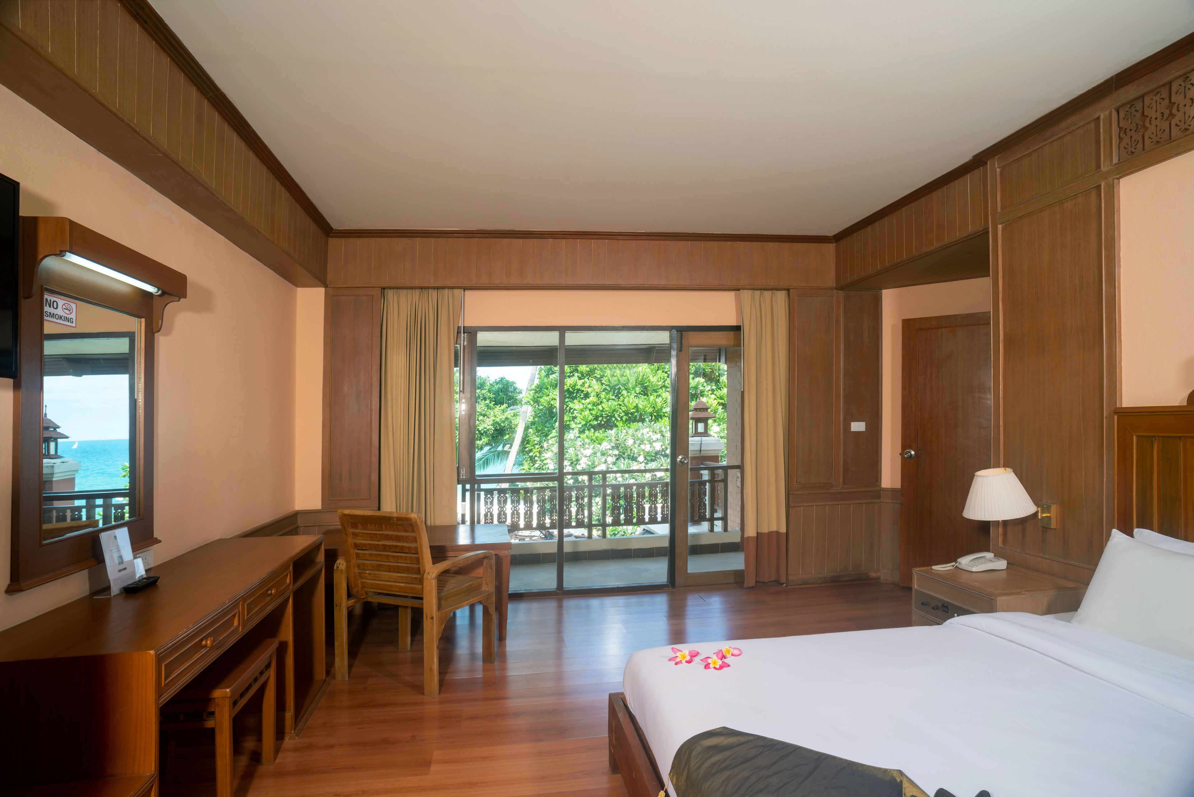 A hotel room with a bed, desk, chair, and a balcony with a view of the sea.