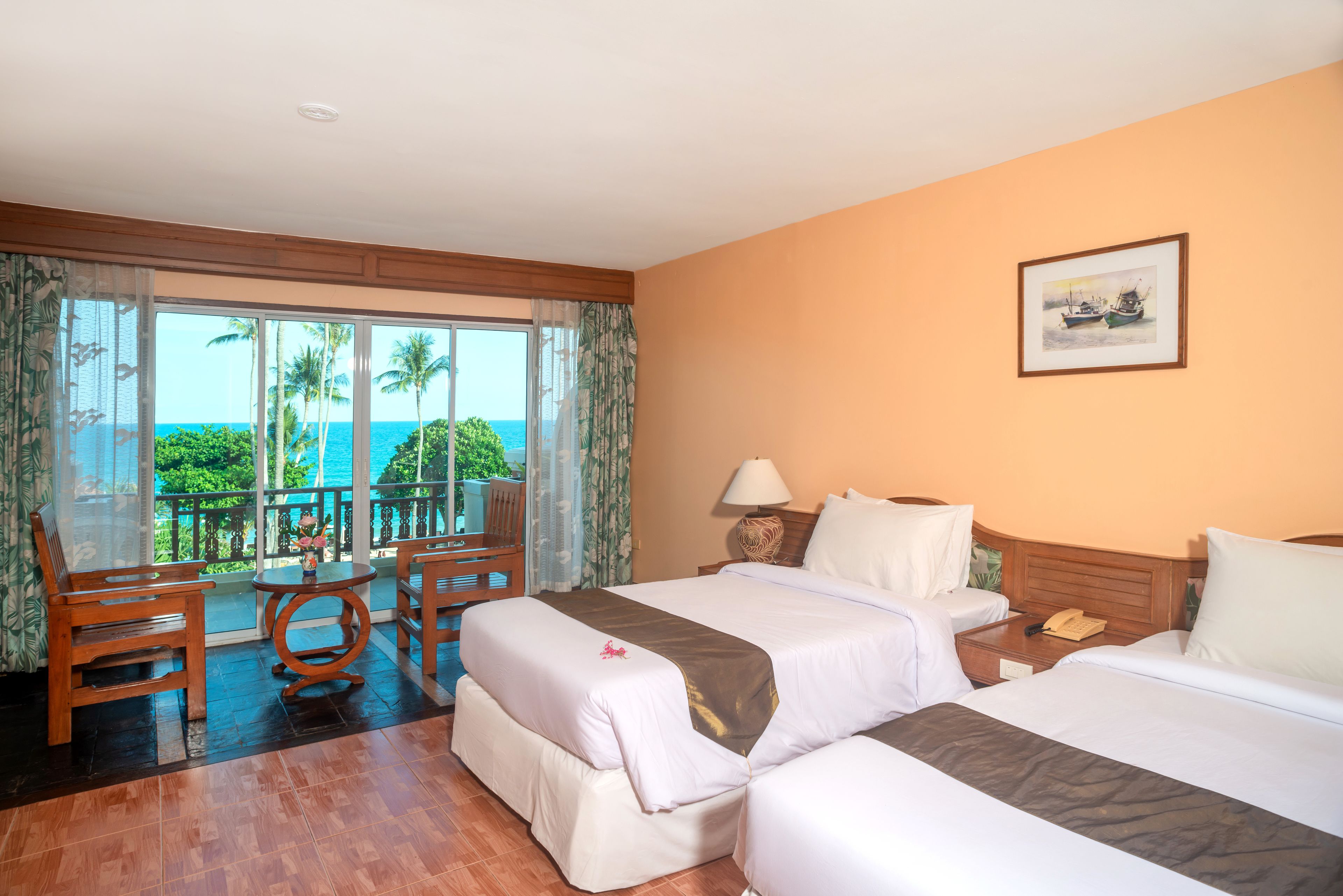 A hotel room with two beds, a balcony with a view of the ocean, a dining table, and a chair.