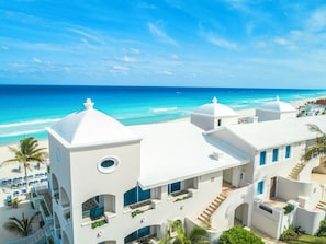 Un bâtiment blanc doté de nombreux balcons, donnant sur une plage et la mer.