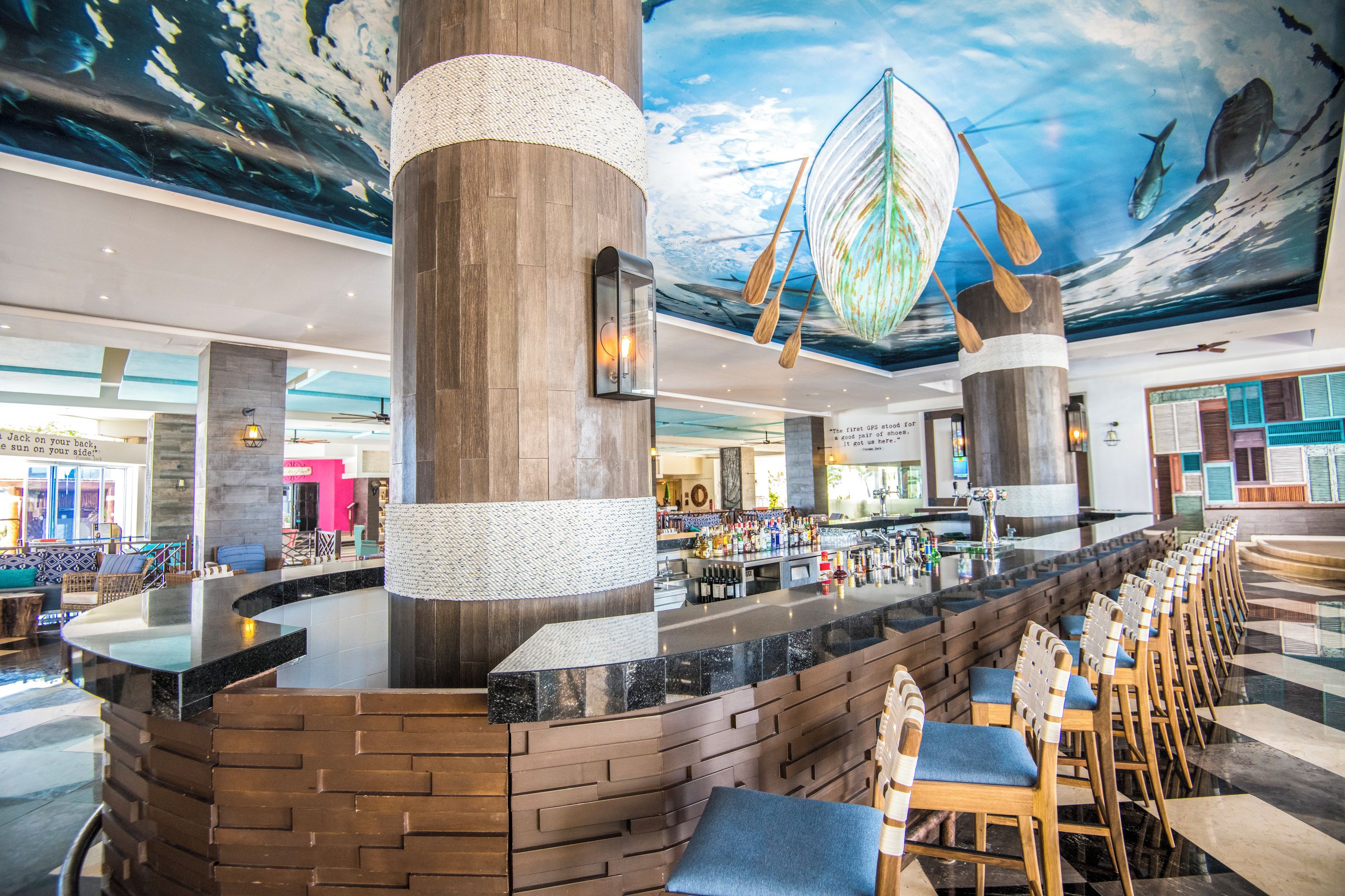 Un grand espace bar doté d’un long comptoir, de chaises en bois et d’une fresque murale au plafond représentant la vie marine.