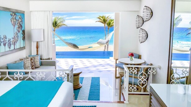 A hotel room with a bed, a desk, a chair, a view of the beach, and a hammock. - Sunscape Cancun Resort & Spa - All Inclusive (Cancun)