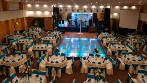 Un salón de banquetes con mesas redondas dispuestas en semicírculo, una pista de baile central con iluminación LED y un escenario con equipo musical.