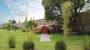 Un jardín bien cuidado con una estructura roja en el centro, posiblemente un pabellón, rodeado por un muro de ladrillo y diversas plantas.