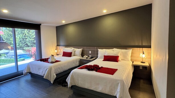 Una habitación de hotel moderna con dos camas, un ventanal grande y techo oscuro.
