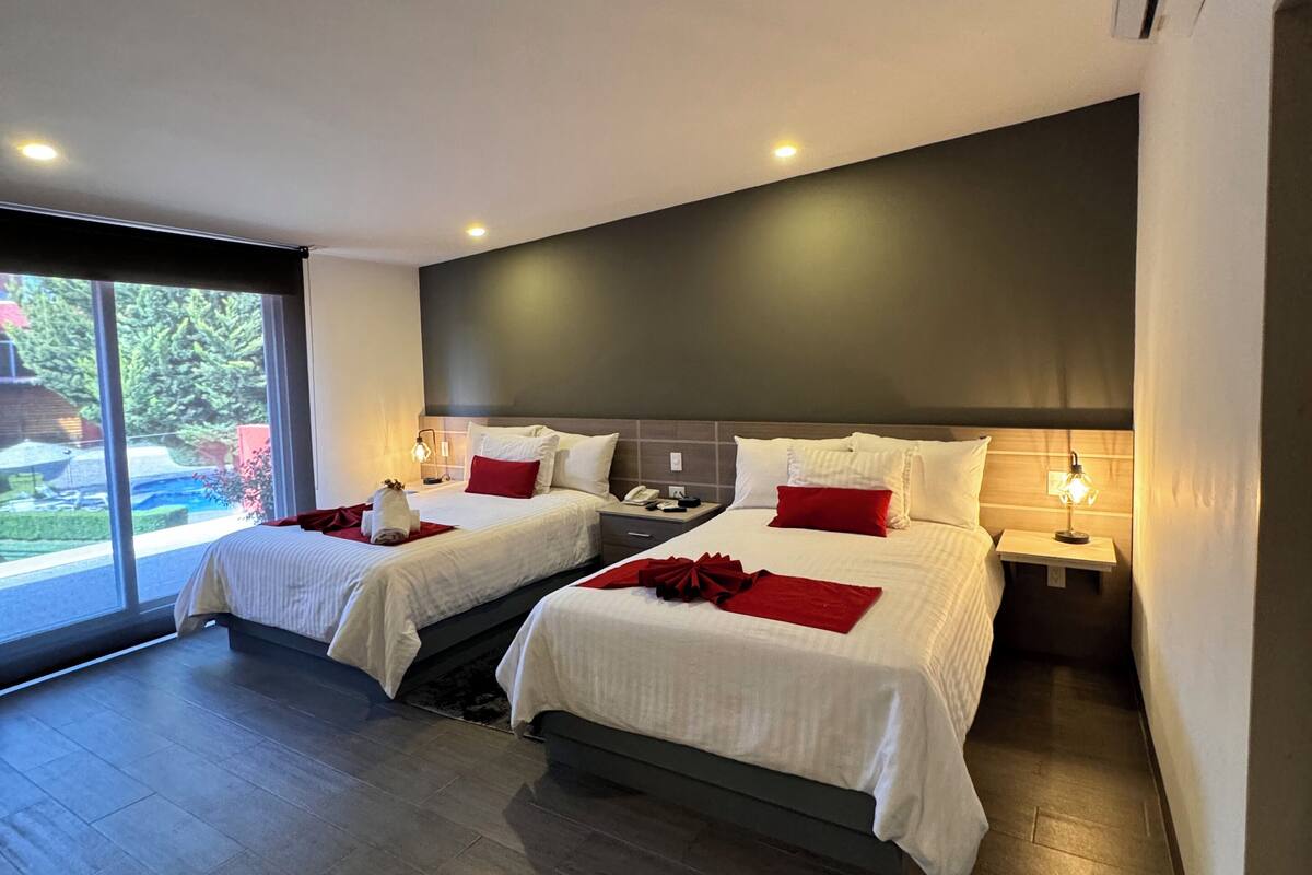 A modern hotel room with two beds, a large window, and a dark ceiling.